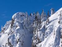 Teleblick zu verschneiten Felswänden und Tannen